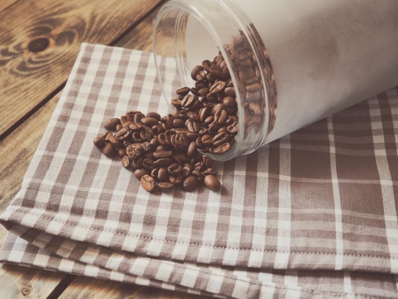 Coffee beans spilling from a jar onto a checked cloth